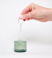 Hand holding a dropper over a fragrance free sensitive skin serum bottle labeled 'FOXTAIL BEAUTY' on a white background