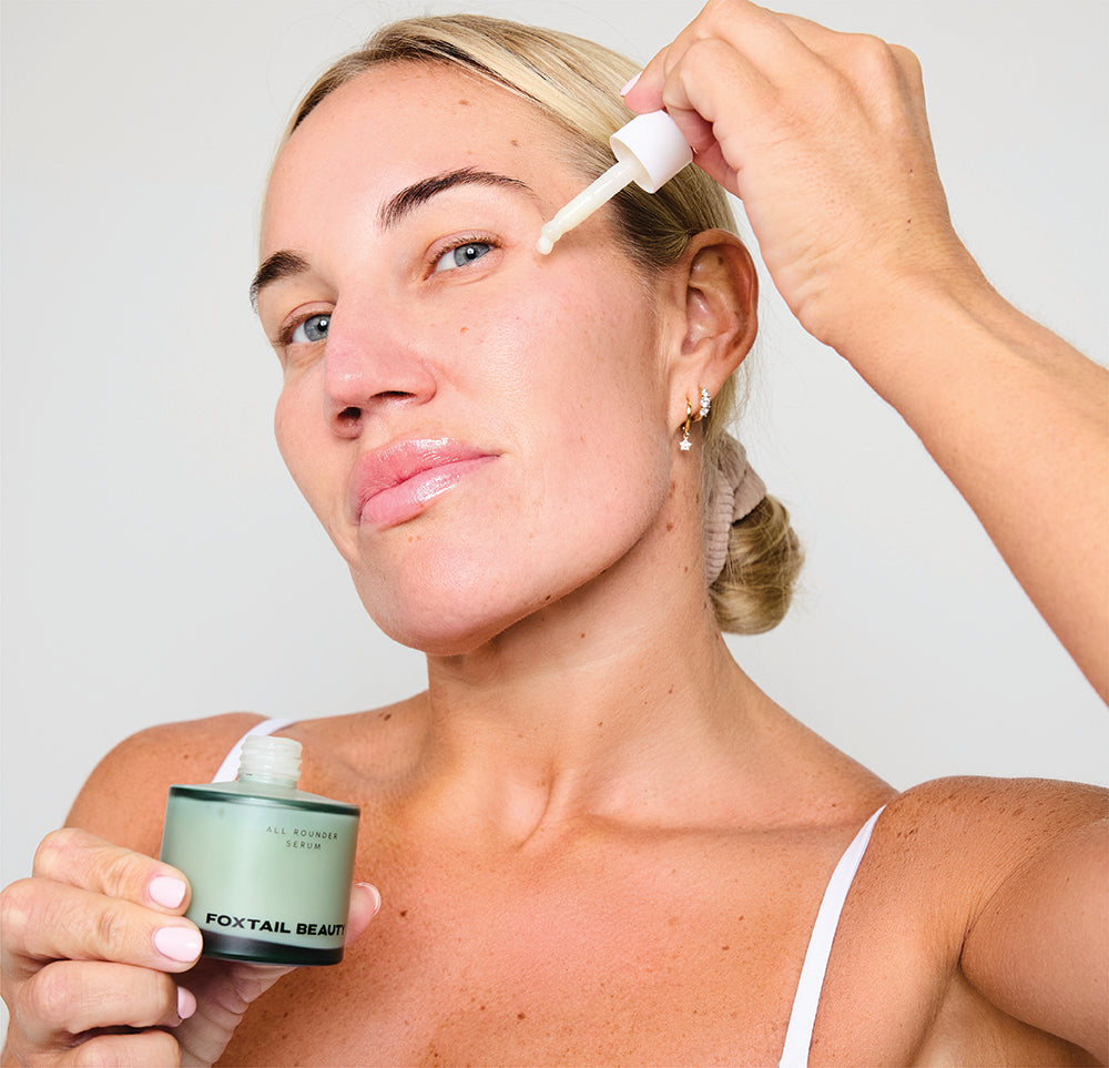 Woman applying a Foxtail Beauty serum for sensitive acne prone skin to her face with a dropper and jar.