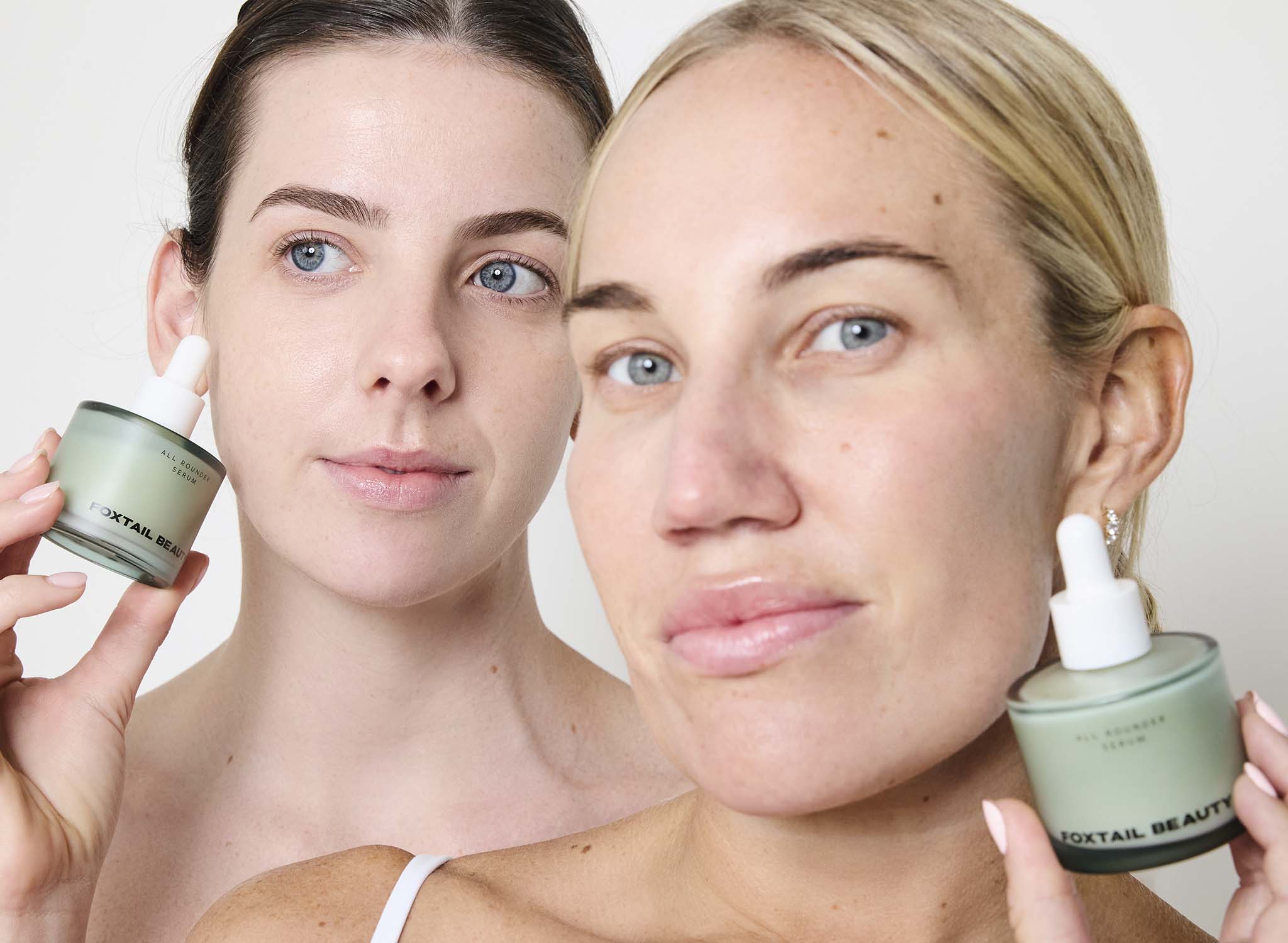 Two women holding bottles of Foxtail Beauty All Rounder Serum product against a plain background